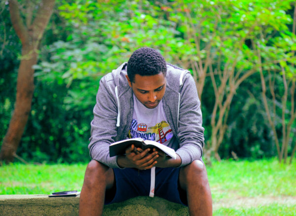 a man wearing a gray sweatshirt sitting outside reading a book