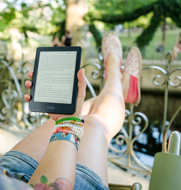 Image of a person reclining outside reading on a Kindle.