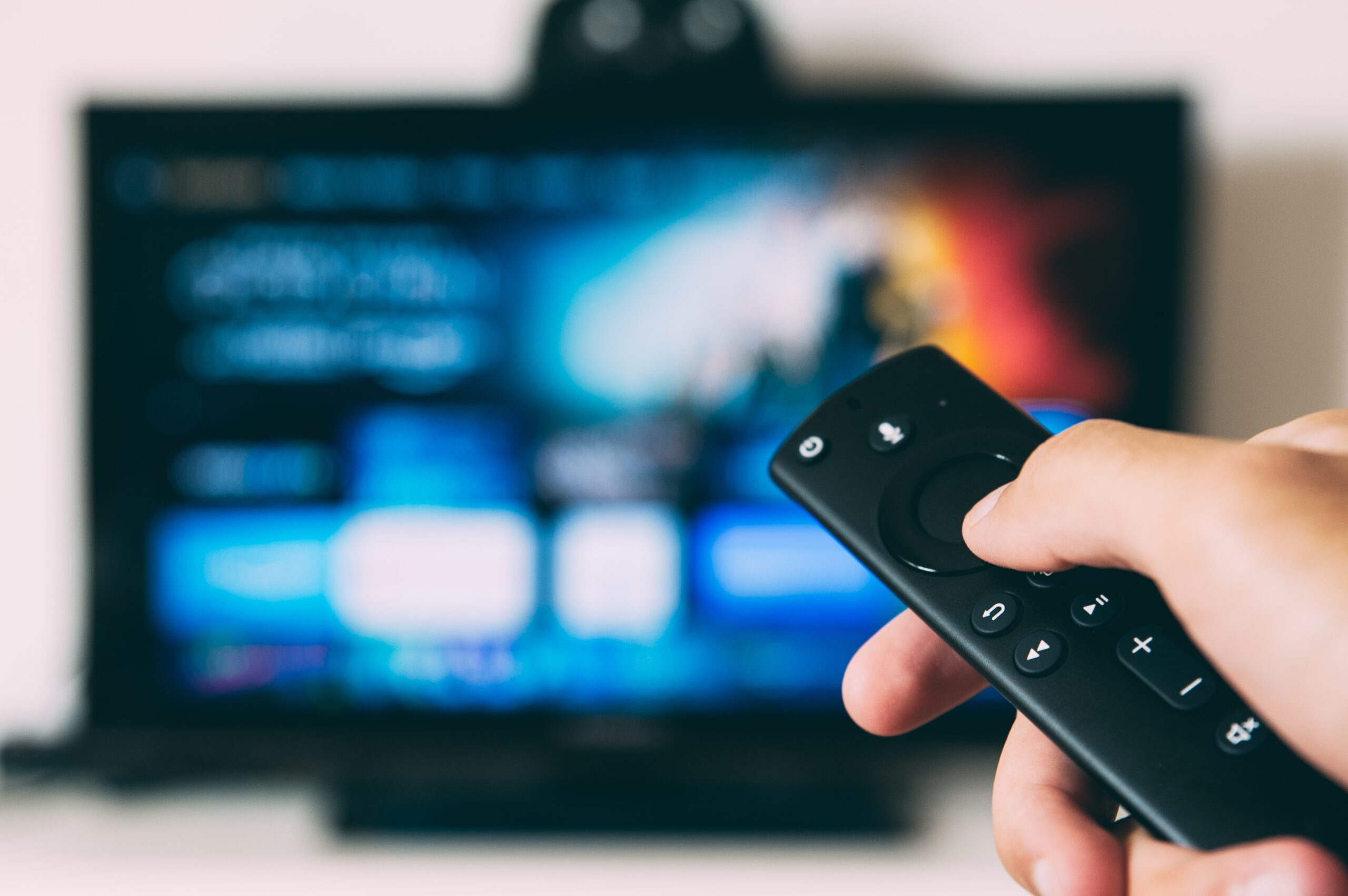 a hand holding a remote control pointing at a TV