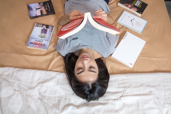 A person reading on a bed surrounded by books