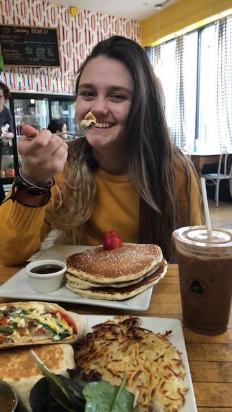 photo of a smiling brunette woman in front of a plate of pancakes