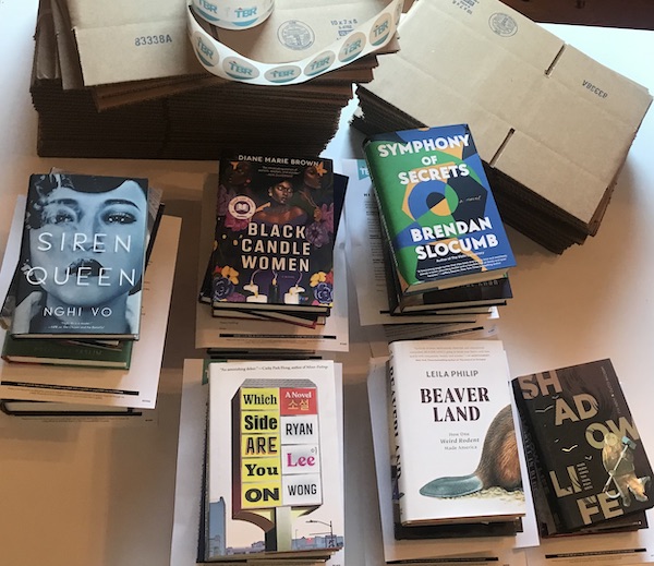 six small stacks of books next to a pile of flattened boxes and a roll of TBR stickers